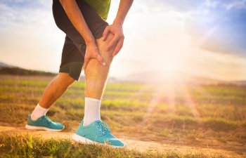 A man is running on a field with his knee hurting.