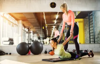 handsome young female instructor helping her client to stretch her arms after hard training in a gym