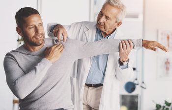 Doctor, man and patient with stretching for shoulder pain with physical therapy, examination or body recovery. Orthopedic, physician or medical expert for arm rehabilitation with healthcare or advice