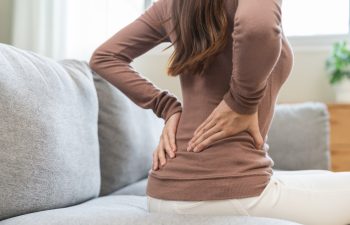 Pain body muscles stiff problem, suffer asian young woman painful back, symptom injury ache from long study work, hand holding massaging or rubbing lower back hurt, sore sitting on sofa at home.